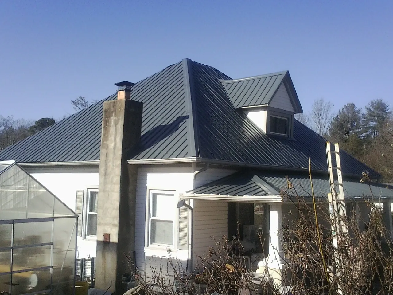 Dark blue standing seam metal roof on a white farmhouse with dormer — Slate & Tile Roof Repair by Roofing Brothers in Hartland