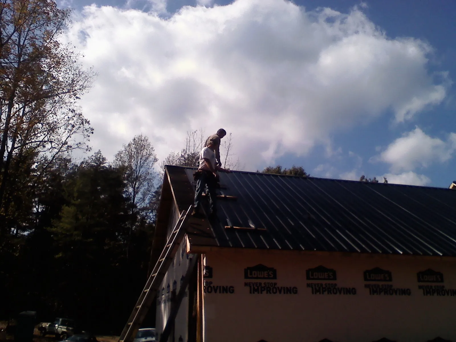 Roofer fastening dark metal panels high against a cloudy sky, from a Roof Inspection job in Hartland