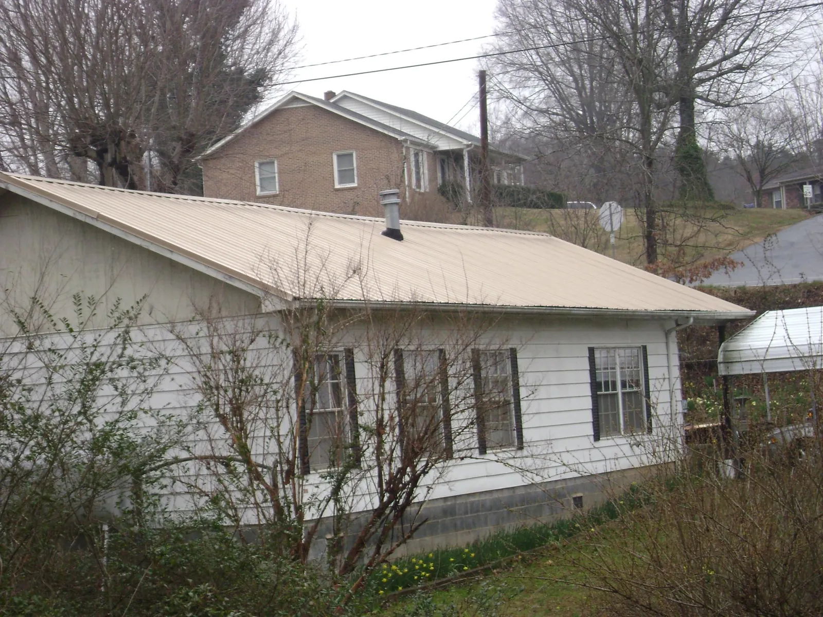 Tan metal roof on a white sided house set into a hillside — Commercial Roofing by Roofing Brothers in Hartland